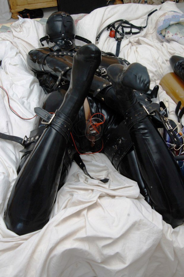 Restrained sub in leather outfit takes a butt plug